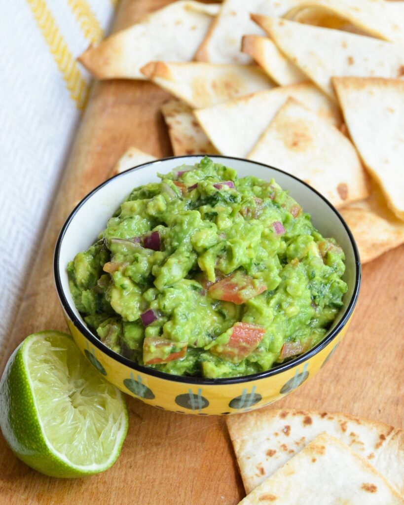 Guacamole in a yellow bowl with half a lime and tortilla chips around.