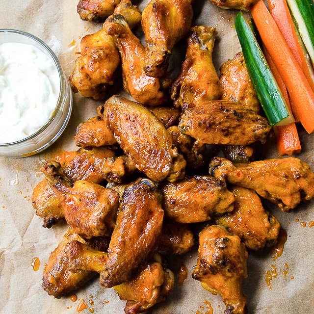 Buffalo Wings on parchment paper with celery and carrot sticks and dip.