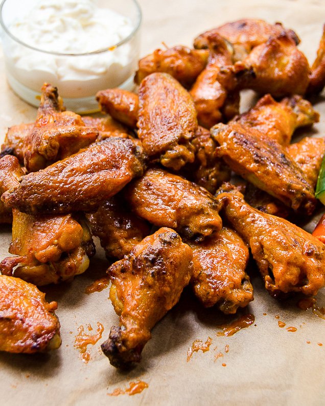 Buffalo Wings on parchment paper with celery and carrot sticks and dip.
