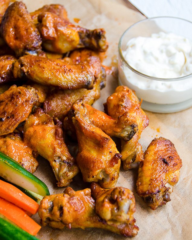 Buffalo Wings on parchment paper with celery and carrot sticks and dip.