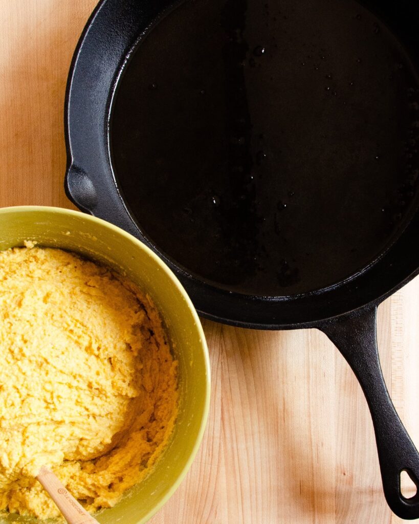 Cornbread batter next to a cast iron pan.