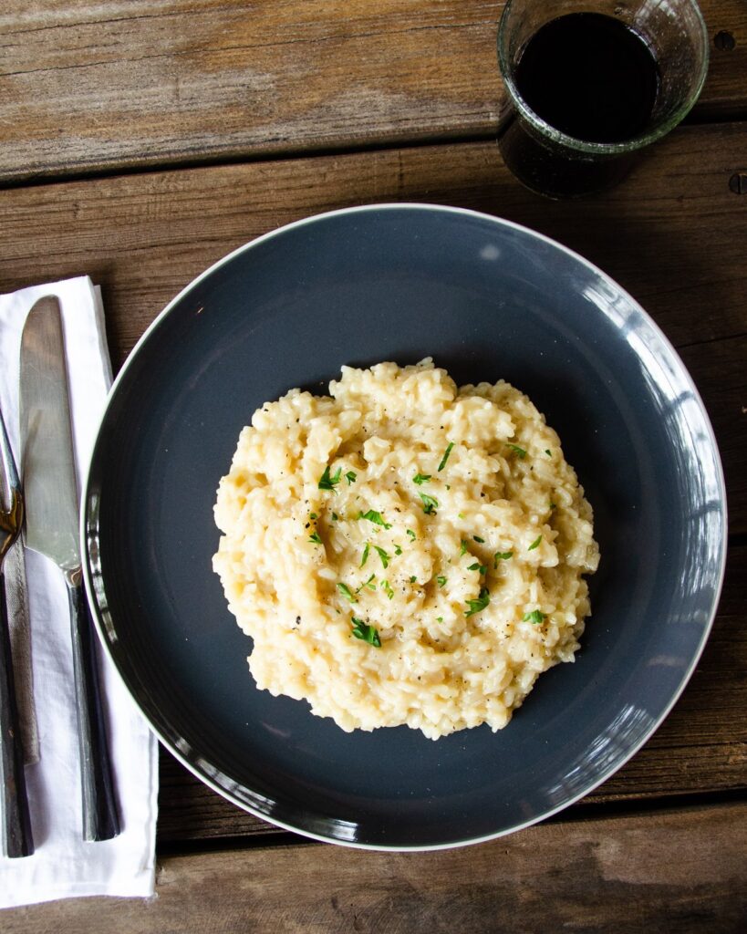 Parmesan risotto on a grey plate with knife and fork and tumbler of wine.