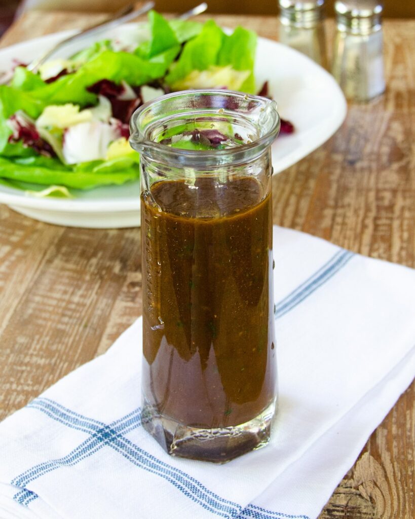 Simple Vinaigrette in a glass cruet with a salad behind.