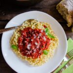 Marinara on curly fusilli in a white bowl with a green napkin, bread and sauce pan of sauce near by.