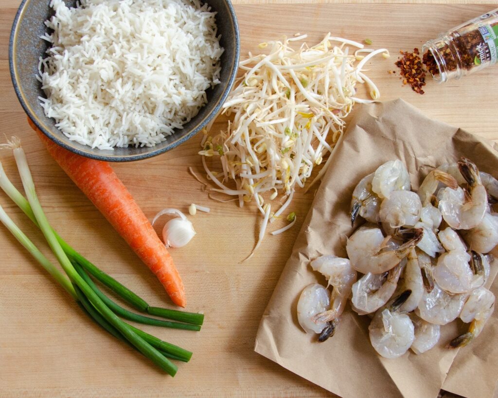 Ingredients for shrimp fried rice on brown paper - shrimp, rice, sprouts, carrot, green onion, carrot.