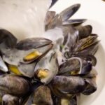 Mussels in a white bowl with cream sauce being poured over.