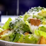 Caesar Salad on a white plate with Parmesan cheese sprinkling down on it.