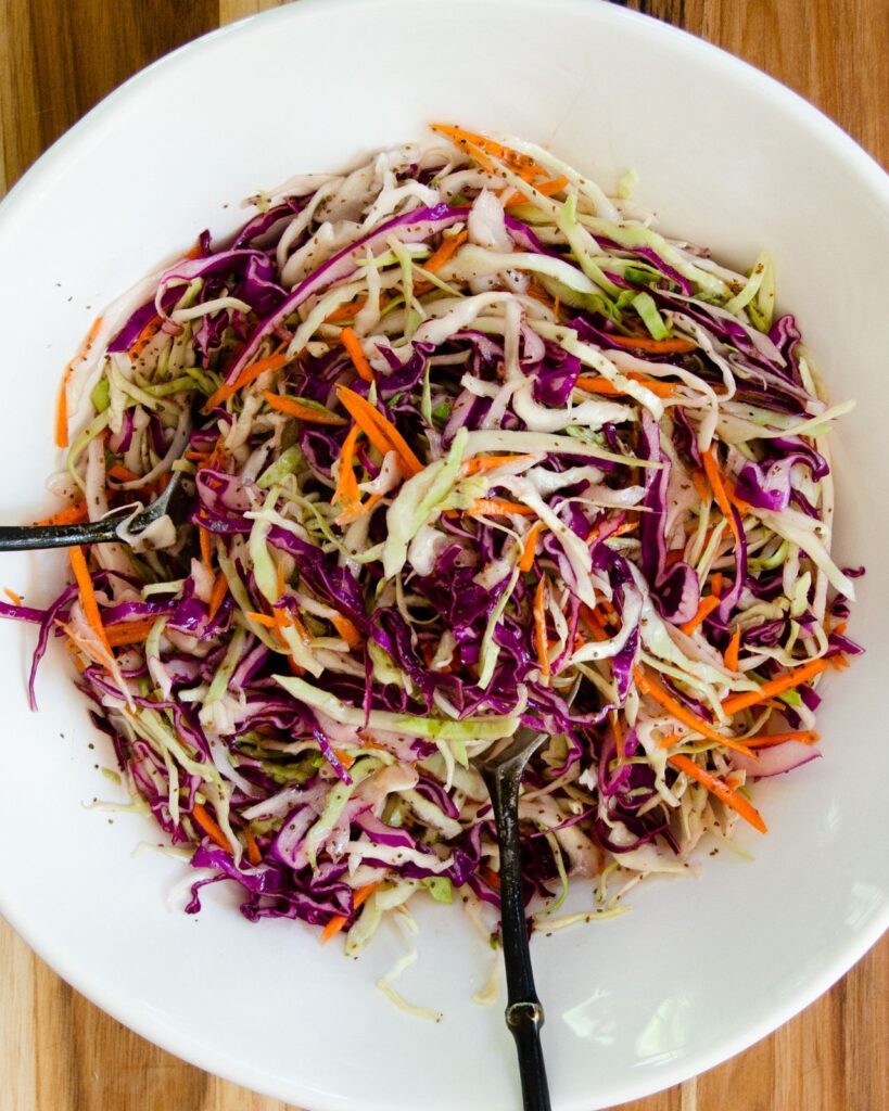 Vinaigrette Coleslaw in a white bowl with metal salad servers.