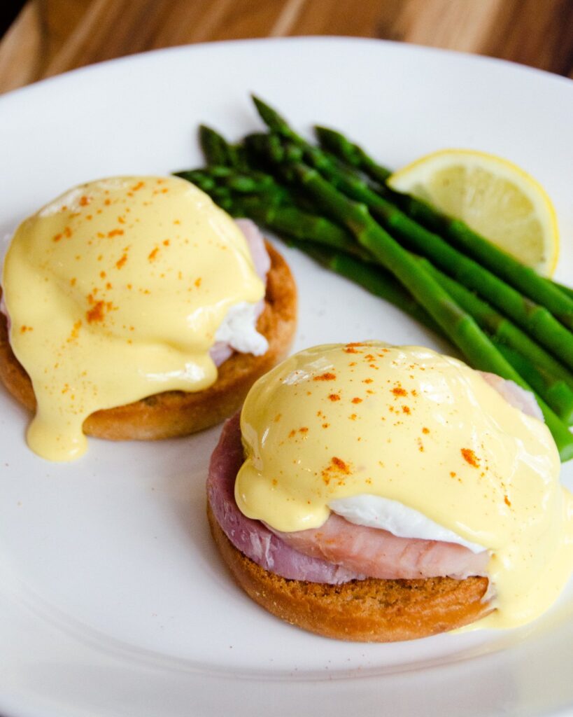 Hollandaise sauce on top of Eggs Benedict on a white plate.