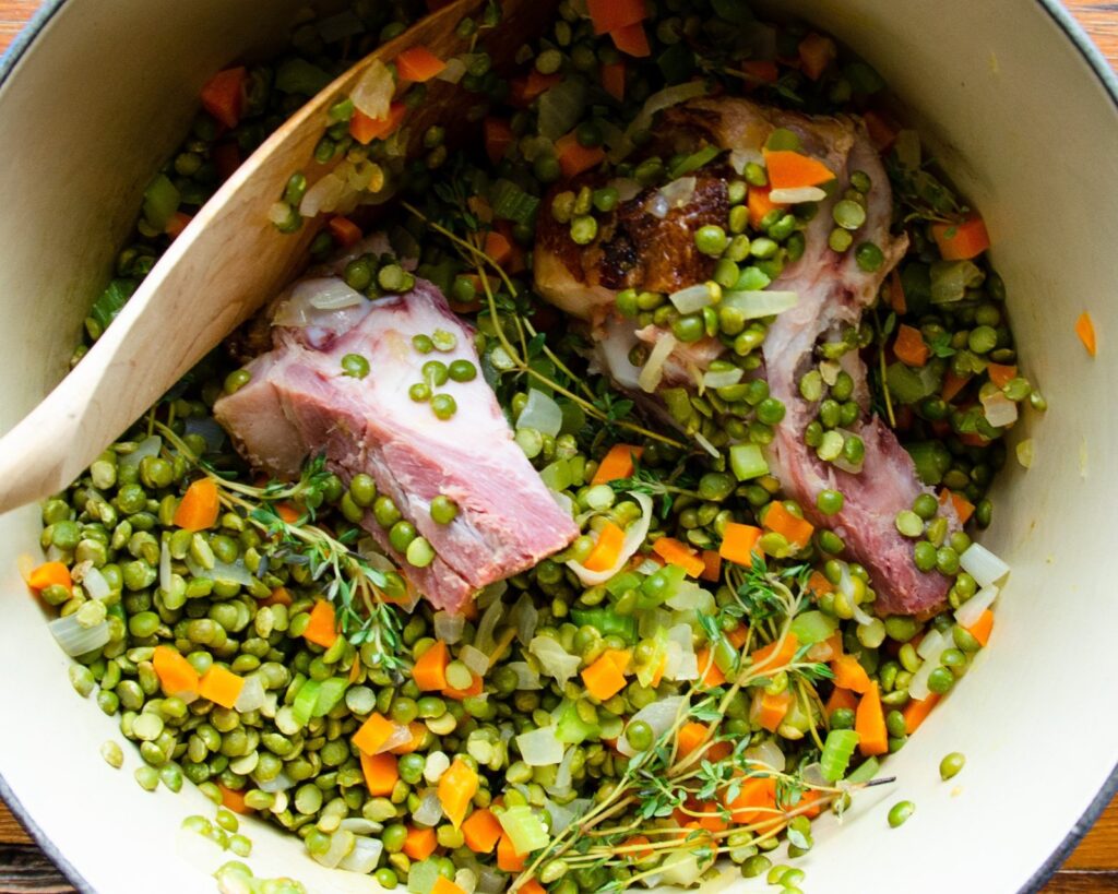 Ingredients for split pea soup in a cast iron Dutch oven - vegetables, ham bone, split peas.