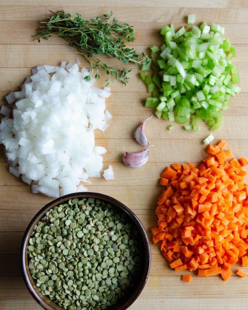 Ingredients for split pea soup on a wooden cutting board - carrots, celery, garlic, thyme, onions and green split peas.