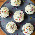 Buttercream frosting piped onto cupcakes on a grey tray on a wooden table.