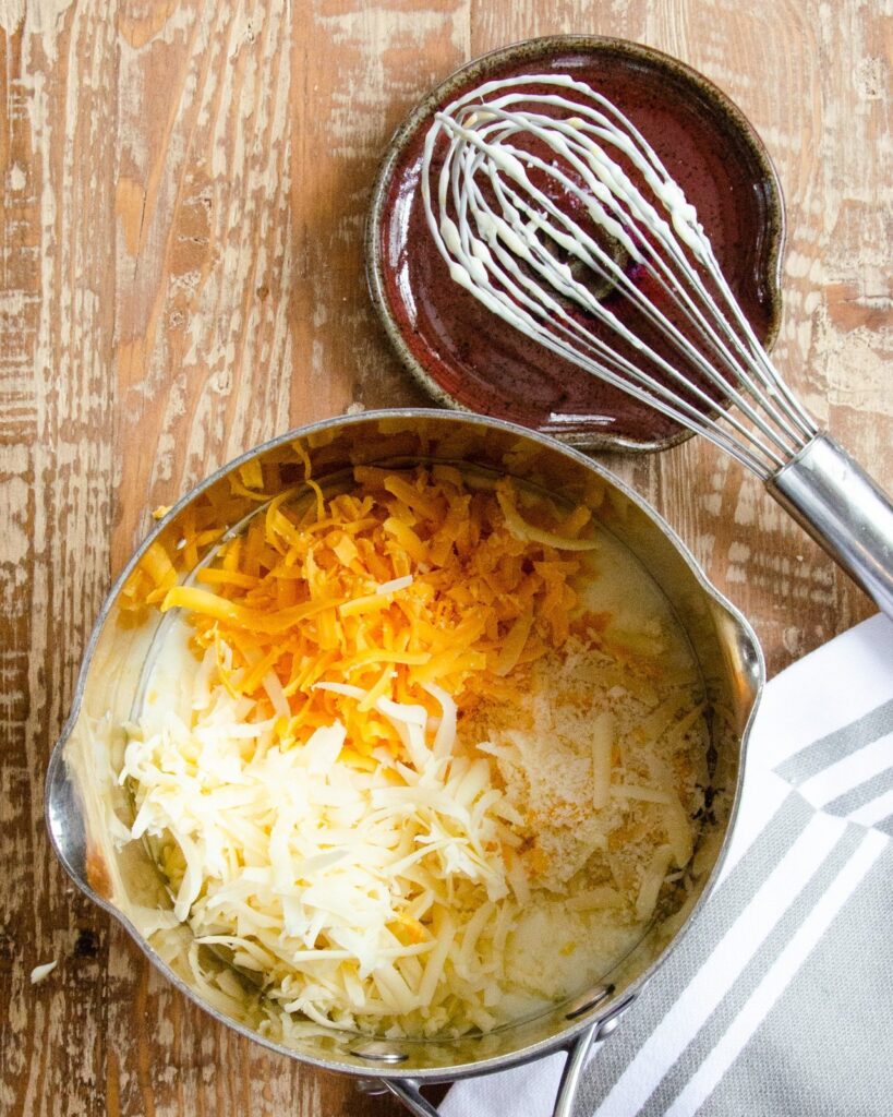 Three cheeses in a saucepan with a whisk on the side.
