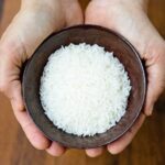 Hands holding a brown ceramic bowl with raw rice.