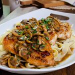 Chicken Marsala over egg noodles on a white platter.