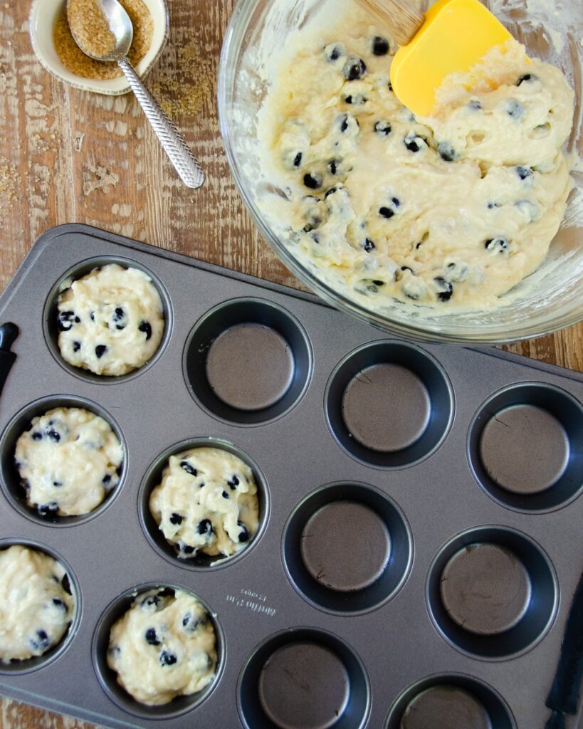 Blueberry muffin batter in a bowl with five cavities filled in a muffin pan.