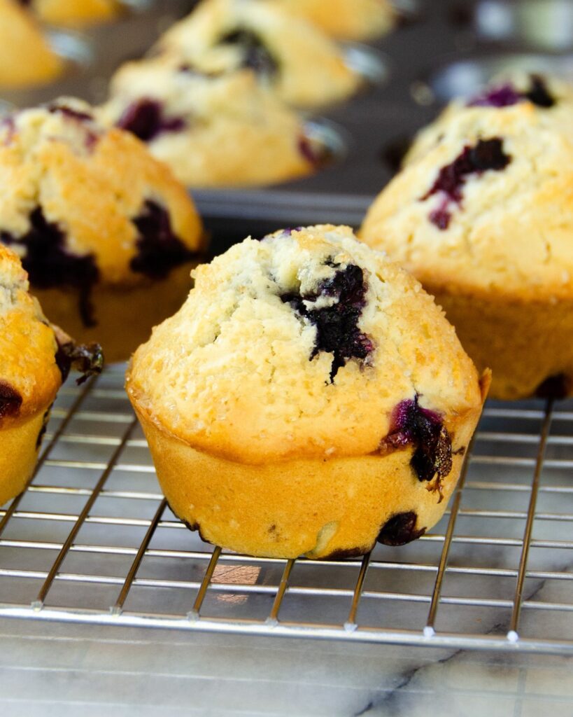 A blueberry muffin on a cooling rack on a marble countertop.