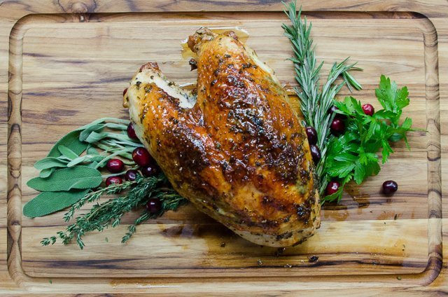 Whole roast turkey breast on a cutting board with herbs and cranberry garnish.