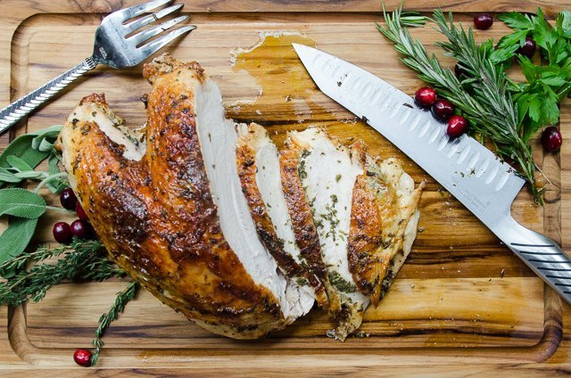 Whole turkey breast, sliced on a cutting board with herbs and cranberry garnish.
