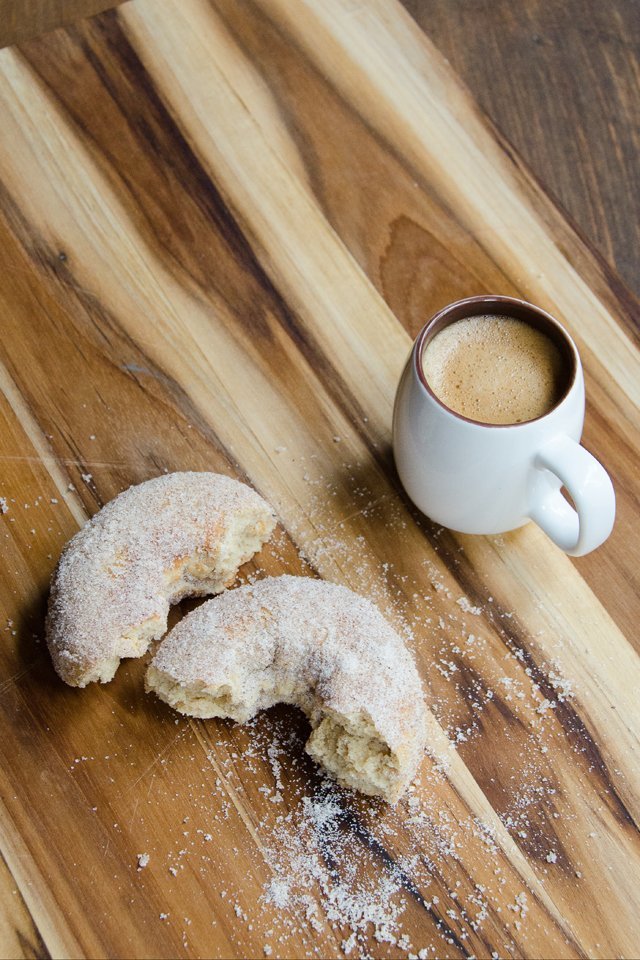 Apple cider doughnuts broken open on a board with a cup of coffee in background.