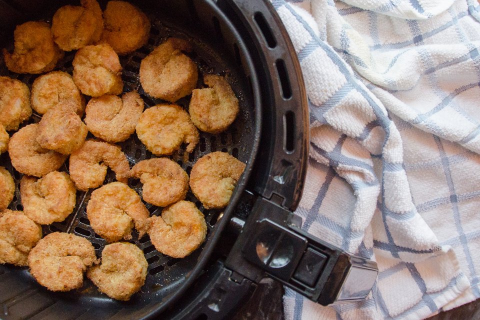 Bang Bang Shrimp in process with coated shrimp in an air fryer basket.