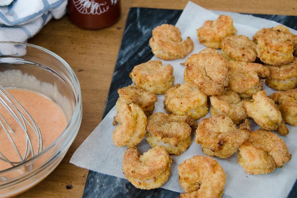 Bang Bang Shrimp in process with the air-fried shrimp on parchment paper and a bowl of bang bang sauce.