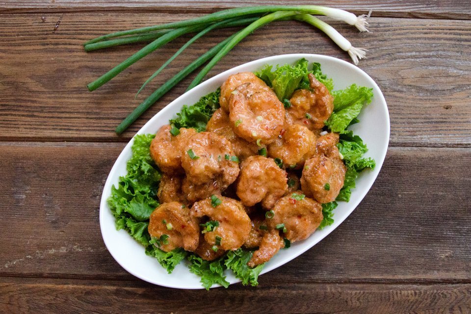 Bang Bang Shrimp on lettuce a white oval platter on a wooden table.