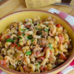Beef and macaroni in a large yellow bowl with parmesan cheese and a grater near by.