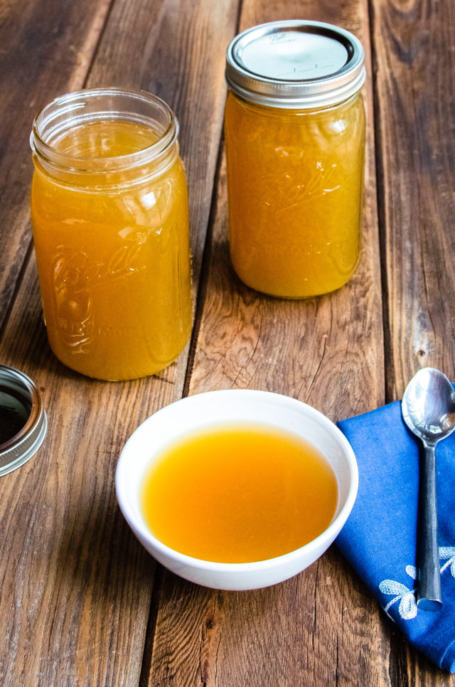 A white bowl of bone broth with two jars of bone broth on a wooden table.