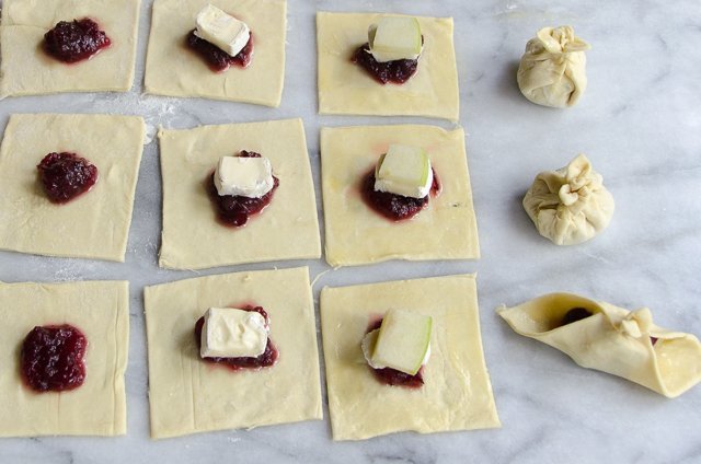 Mini Brie bites in progress: puff pastry squares on marble, with cranberry, Brie and apple.