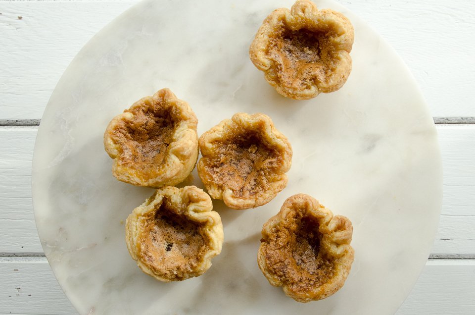 Five Butter Tarts on a marble cake stand on a white wooden table.
