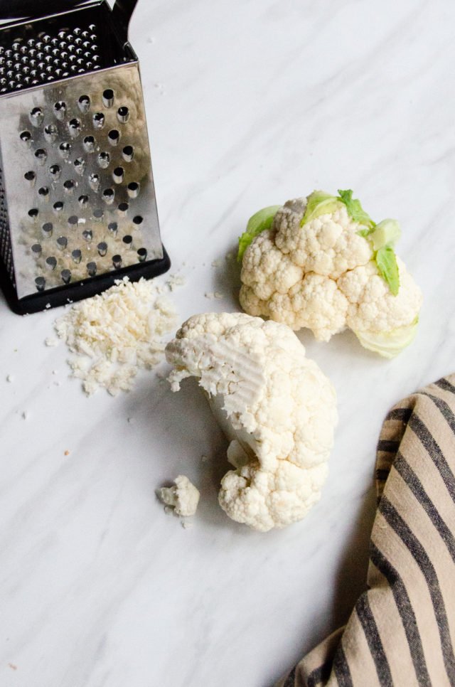 Cauliflower being grated on a box grater on a countertop.