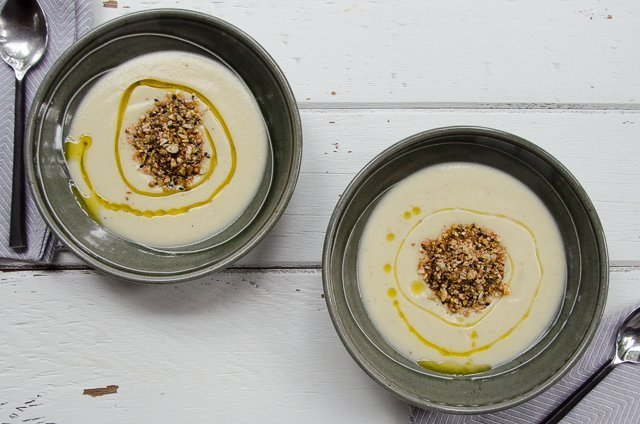 Two bowls of Cauliflower Cheddar Soup on a white wooden table.