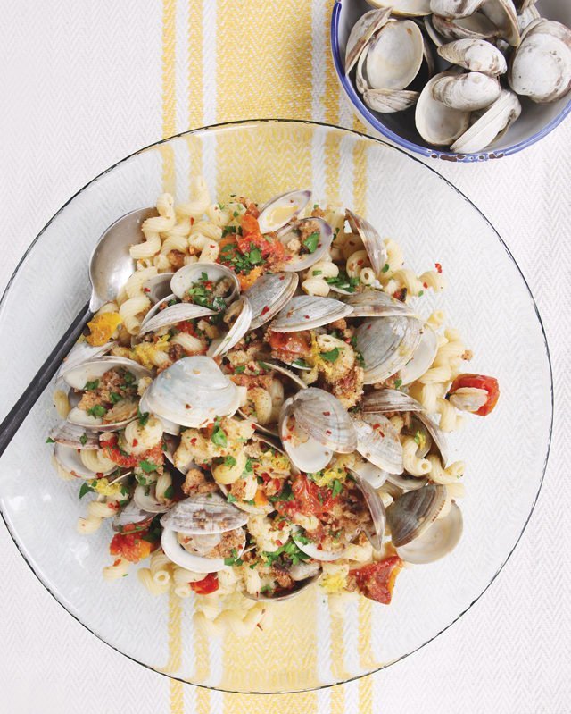 Cavatapi con Vongole in a glass bowl on a tablecloth with a yellow line with empty clam shells nearby.