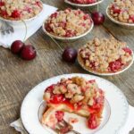 Cherry Streusel tartlets on a wooden table with one partially eaten on a plate with a fork.