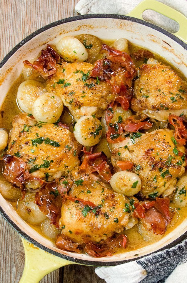 Overhead shot of braised chicken thighs with cipollini onions in a light green cast iron pan.
