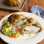 chicken wellington on a white plate on a wooden table with a baking sheet in the background.