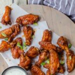 Chipotle BBQ Chicken Wings on parchment paper on a wooden tray with dipping sauce.