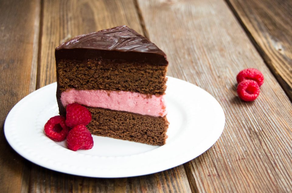 Chocolate Cake on a white plate with raspberry garnish.