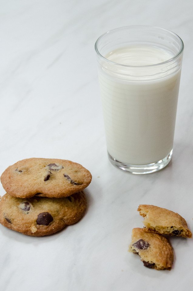 Chocolate chip cookies and a glass of milk on a marble counter.
