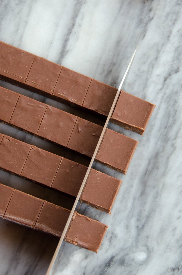 Basic Chocolate Fudge being cut into cubes on a marble counter.