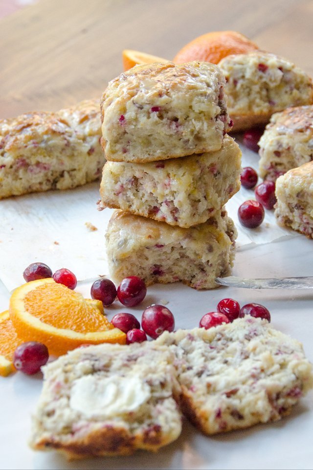 A stack of cranberry orange pecan buttermilk biscuits with one broken open and buttered in front.