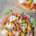 Peach, Prosciutto and Burrata Flatbread on parchment paper on a wooden table.