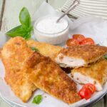 Chicken cutlets on white plate garnished with tomatoes and basil leaves.