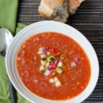 Bowl of Gazpacho with crusty bread, a green napkin and a spoon.