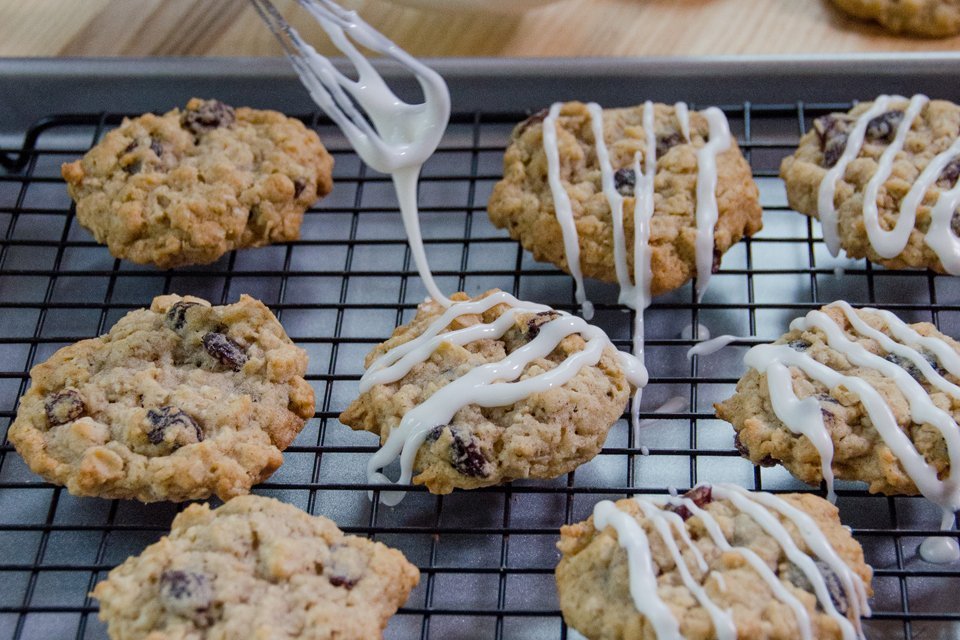 Iced Oatmeal Raisin Cookies being iced on a cooling rack on a wood counter.