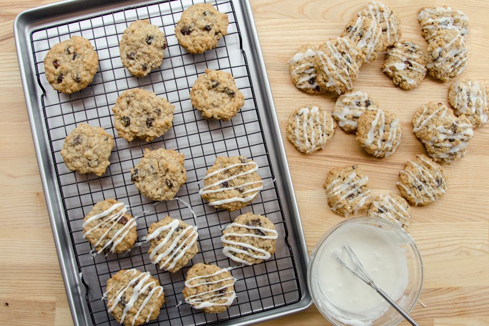 Iced Oatmeal Raisin Cookies being iced on a cooling rack on a wood counter.