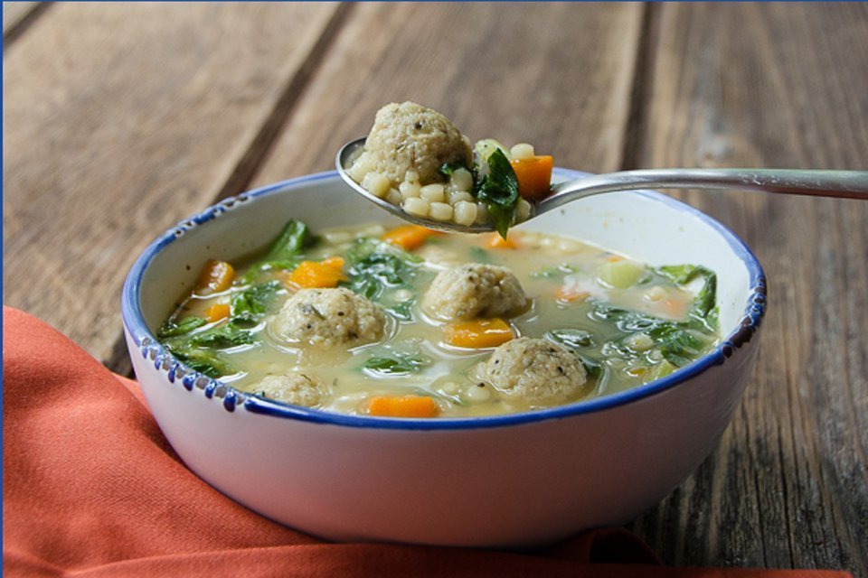 Close up of a bowl of Italian Wedding Soup with a spoon lifting out a meatball.