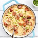 Kielbasa, Pierogies and Sauerkraut Bake in a light blue cast iron pan with spoon.