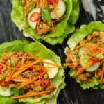 Three Korean BBQ Chicken Lettuce Wraps on a piece of black marble.